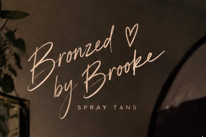 The Bronzed by Brooke spray tans script logo on the studio wall, beside the tanning booth
