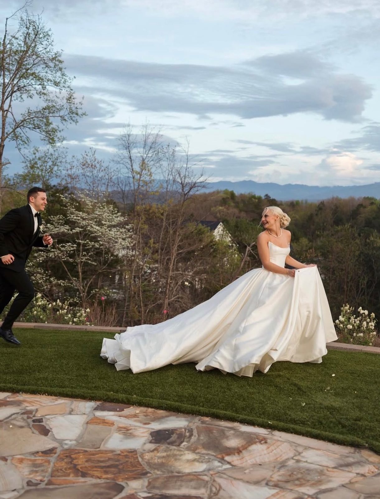 Bride in a full white ball gown on a lawn above the hills