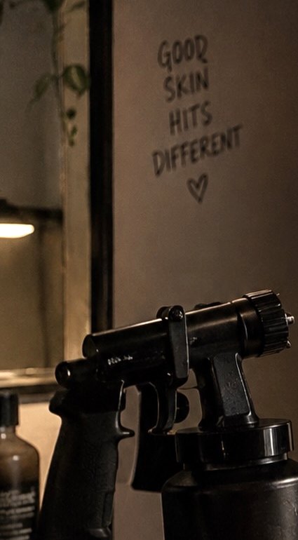 Brooke's studio: a spray tan gun on folded towels, with Good Skin Hits Different written on the wall